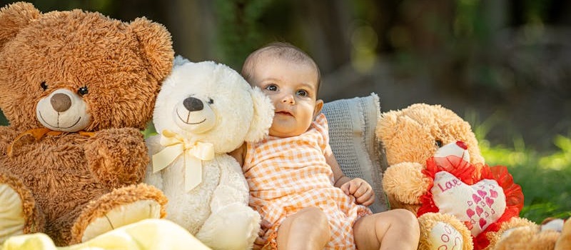 bebé sentado no chão, rodeado de ursos de peluche de várias cores
