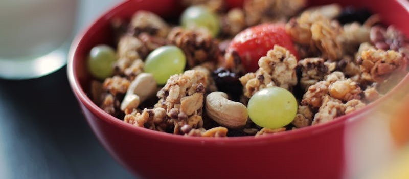 tigela vermelha com cereais, frutos secos, uvas brancas e morangos